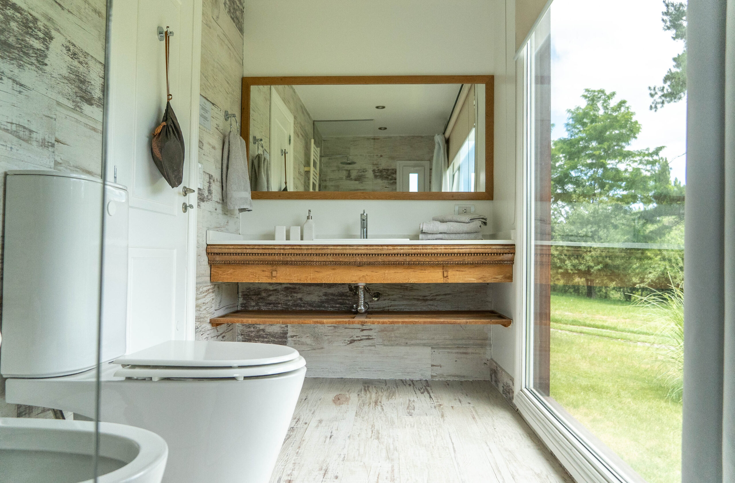 Baño en La Aguada Suite con espejo grande, vanitory y ventanal con vista al jardín en El Bolsón