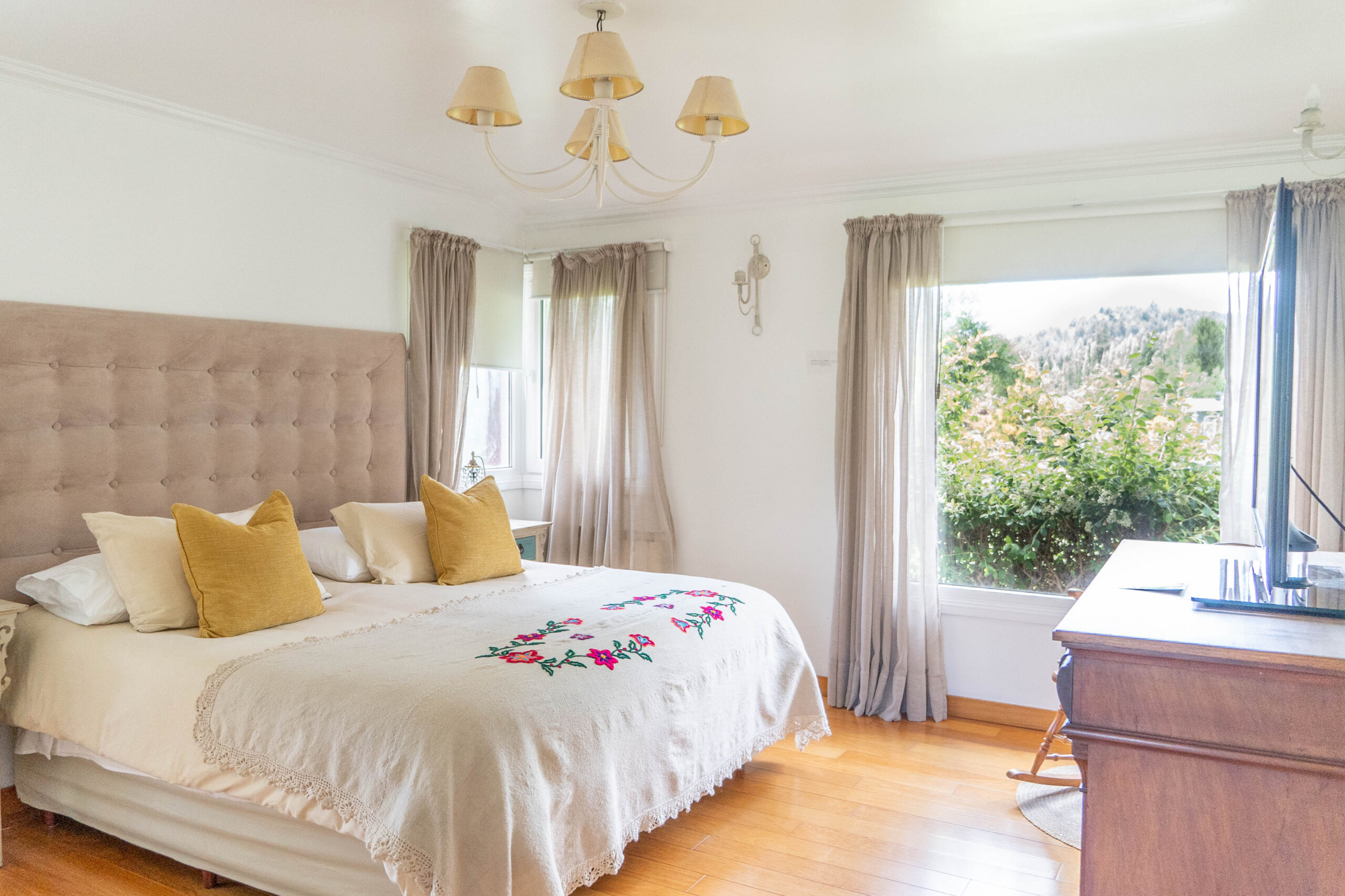 Dormitorio luminoso en La Aguada Suite, El Bolsón, con cama amplia, almohadones, TV y vista al jardín